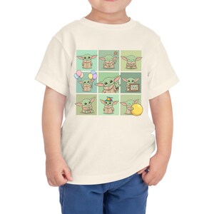 May include: Cream-coloured toddler t-shirt featuring a grid of nine cartoon images of a green alien character. Each image shows the character in different poses, some holding objects like balloons and a ball. The shirt is made of a soft material.