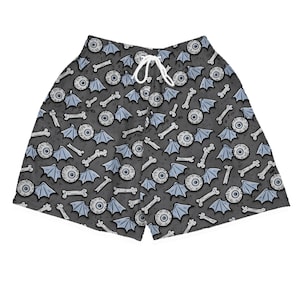 Puede incluir: Pantalones cortos grises con un patrón repetido de globos oculares, huesos y alas de murciélago de dibujos animados. Los pantalones cortos tienen un cordón blanco. El diseño es en tonos grises y azul claro.