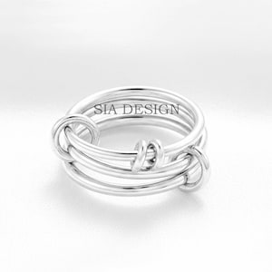 Puede incluir: Un anillo plateado con un diseño único. El anillo presenta múltiples bandas y nudos decorativos. El texto "SIA DESIGN" es visible en el anillo. Esta joya es adecuada para el uso diario.