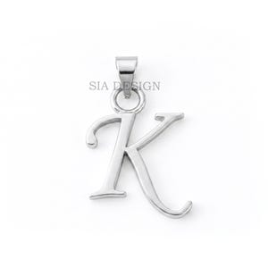 Op de afbeelding: Een zilverkleurige metalen hanger in de vorm van de letter K, uitgevoerd in een cursief lettertype. De hanger is voorzien van een klein rond oogje aan de bovenzijde voor bevestiging. De tekst SIA DESIGN staat in een klein, donker lettertype erboven.