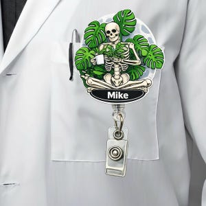 May include: A retractable badge reel featuring a skeleton meditating with a cup, surrounded by green leaves. The name "Mike" is printed on a black oval. The reel is attached to a silver clip.