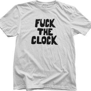 May include: White t-shirt with the phrase "FUCK THE CLOCK" printed in bold, black letters. The text is centered on the front of the shirt. The shirt has short sleeves and a crew neck.