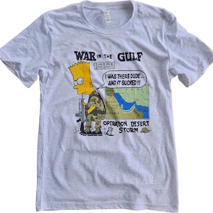 Może przedstawiać: Jasnoszara koszulka z Bartem Simpsonem w mundurze wojskowym, trzymającym karabin, z napisem "WAR IN THE GULF 1991" i "I WAS THERE DUDE... AND IT SUCKED!!!" Widoczna jest również mapa Zatoki Perskiej. Koszulka ma okrągły dekolt.