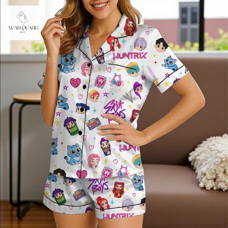 A woman wearing a white pajama top with a cartoon character print, posing in a room with a couch and a window.