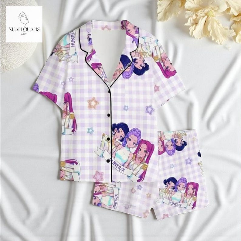 A pair of pajama bottoms with a cartoon-style design featuring multiple characters, including a girl with purple hair and a boy with a bow in his hair. The pajamas are displayed on a white background, and there are some flowers visible in the background.