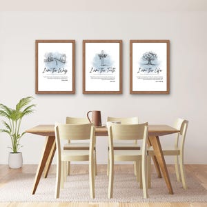 May include: Three framed art prints with watercolor illustrations and text. The prints, in wooden frames, display the phrases "I am the Way," "I am the Truth," and "I am the Life." The artwork is displayed above a wooden dining table with chairs.