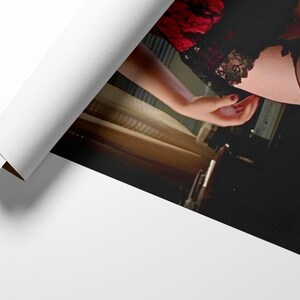 May include: A rolled-up print showing a woman in black lingerie with red lace detailing. The image includes a hand with red nail varnish. The print is partially unrolled, revealing the image.