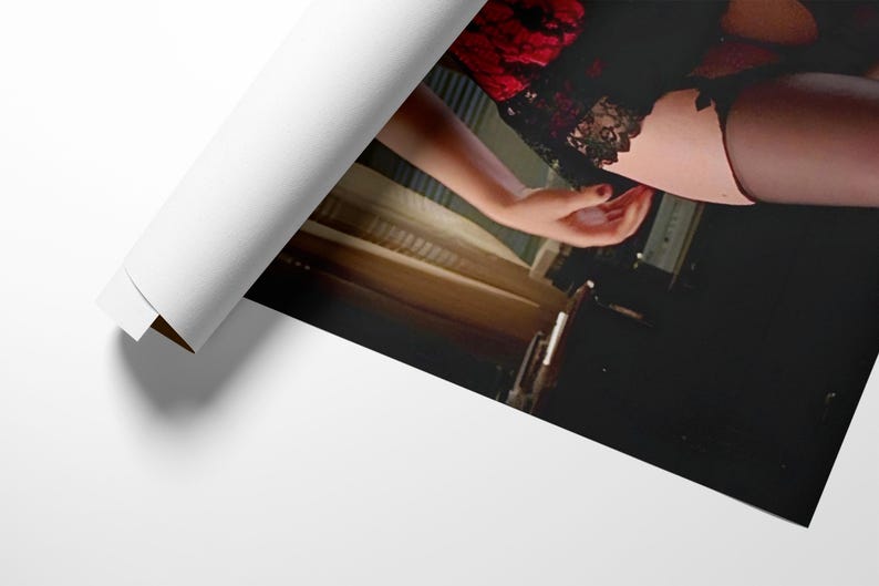 May include: A rolled-up print showing a woman in black lingerie with red lace detailing. The image includes a hand with red nail varnish. The print is partially unrolled, revealing the image.