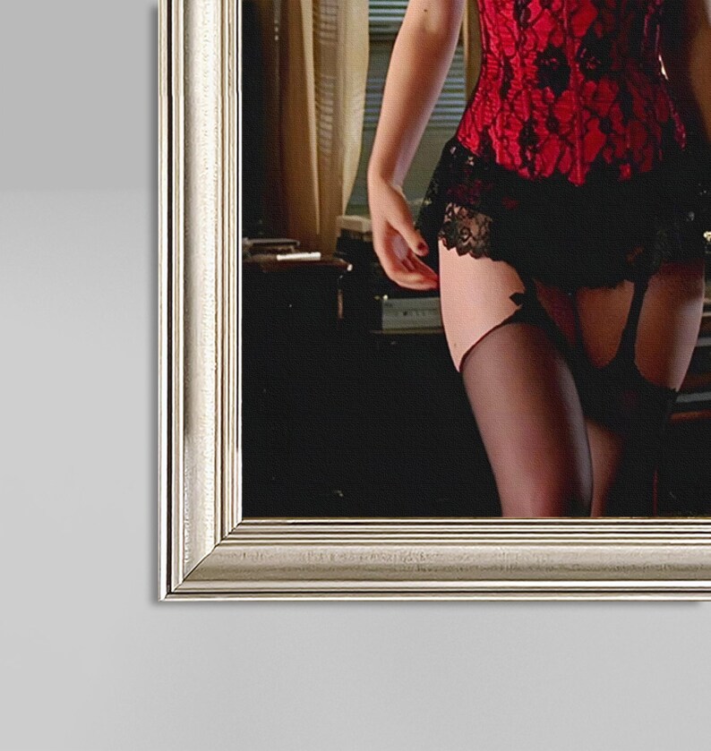 May include: A framed image showing a red lace corset with black lace detailing, worn with a black skirt and stockings. The image is framed in a silver-coloured frame, enhancing the overall aesthetic.