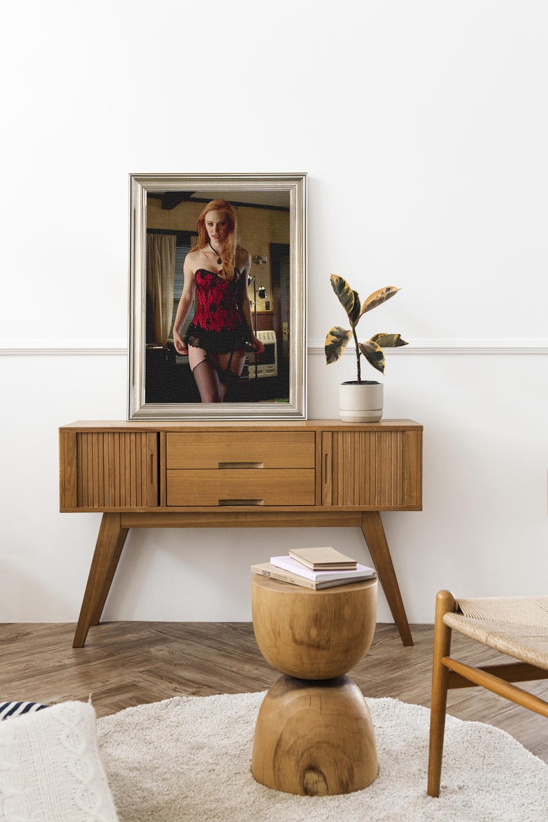May include: A wooden cabinet in a mid-century modern style, featuring two doors, two drawers, and angled legs. A mirror above reflects a person in a red and black corset. A small wooden stool and a potted plant are also visible in the room.