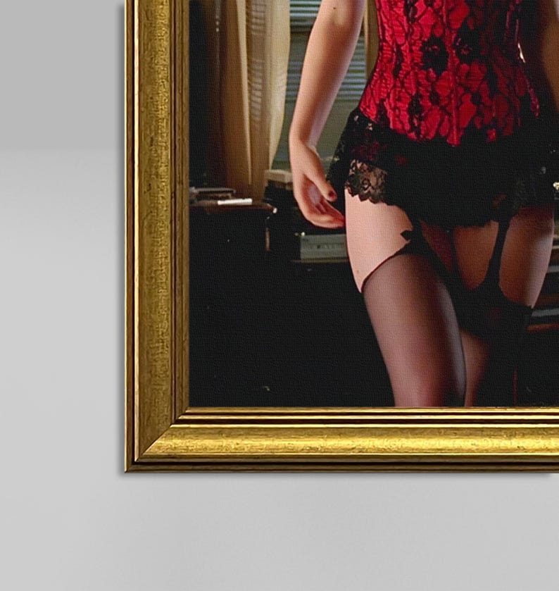 May include: A framed image showing a red lace corset with black lace trim and a matching skirt. The model is wearing black stockings with garter straps. The frame is gold.