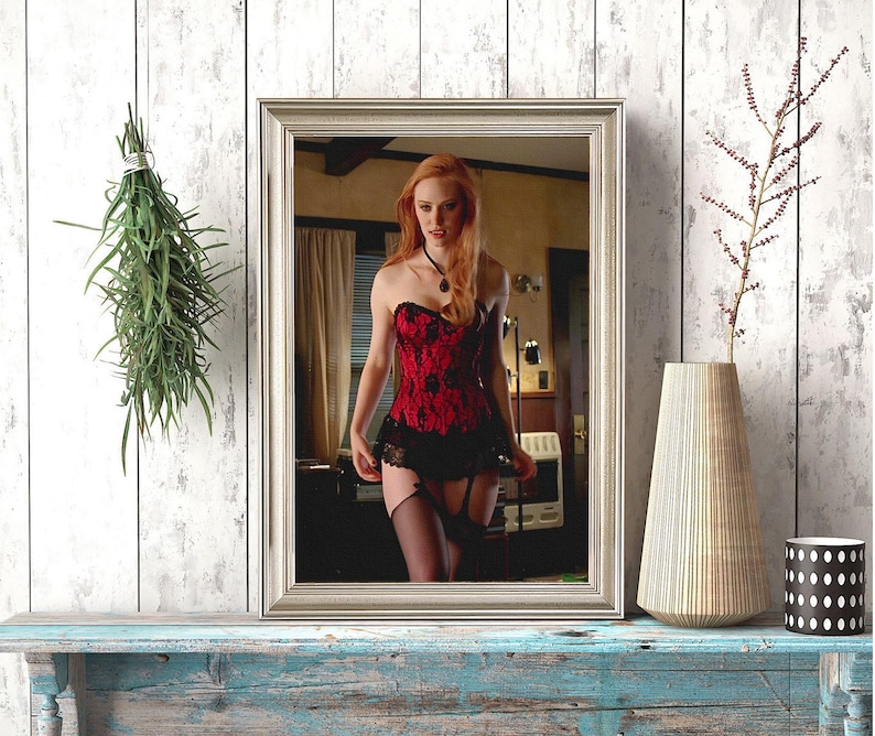 May include: A silver-framed mirror reflects a person in a red and black corset and black stockings. The mirror sits on a distressed blue wooden surface. A vase and a black and white polka-dot container are also on the surface.