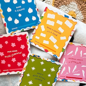 May include: A collection of colorful reward cards with various activities written on them, including "Bake a treat," "Read a chapter in a book," and "Journal about a gratitude." Each card has a unique color and design.