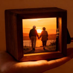 May include: A wooden box with a framed image of an elderly couple walking towards a sunset. The box has a crank on the side. The image is illuminated from within, creating a warm, inviting glow.