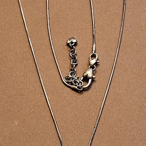 Puede incluir: Collar plateado con dos colgantes. Uno tiene forma de l&aacute;grima con la palabra "LOVE" y un coraz&oacute;n. El otro es un coraz&oacute;n cubierto de peque&ntilde;as piedras. El collar tiene una cadena fina.