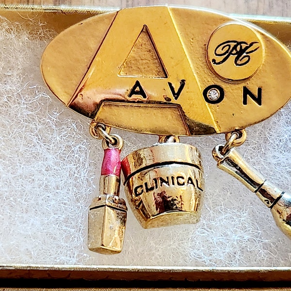 Vintage Avon award brooch with makeup charms dangling.