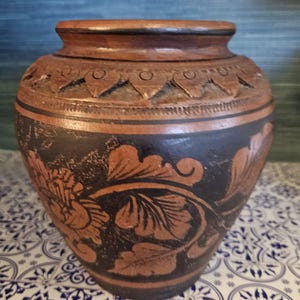 Könnte beinhalten: Eine braune Keramikvase mit schwarzen und braunen floralen Designs. Die Vase hat eine breite Öffnung und einen runden Körper.