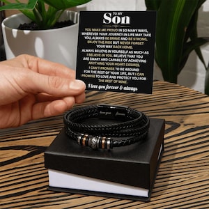 May include: Black braided leather bracelet with silver and rose gold accents, presented in a black gift box. A card with the text "To My Son" and a heartfelt message is held above the bracelet. The bracelet has the words "love you forever" engraved on it.