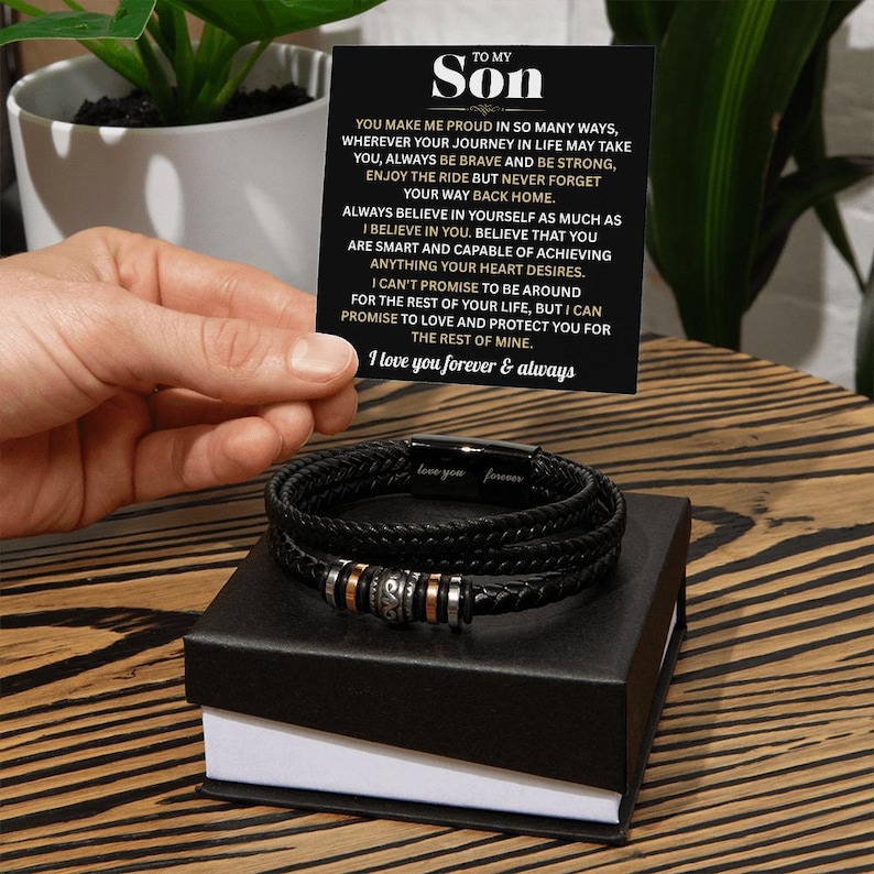 May include: Black braided leather bracelet with silver and rose gold accents, presented in a black gift box. A card with the text "To My Son" and a heartfelt message is held above the bracelet. The bracelet has the words "love you forever" engraved on it.