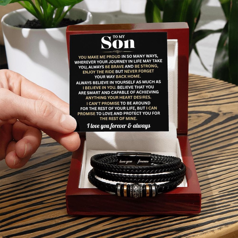 May include: A black braided leather bracelet with silver and gold accents, presented in a red wooden box. The box contains a card with the text "TO MY SON" and a heartfelt message. The bracelet is inscribed with "love you forever".