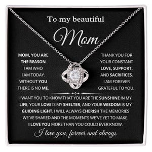 May include: A silver necklace with a pendant featuring a central clear crystal surrounded by smaller crystals. The necklace is presented on a black background with text that reads "To my beautiful Mom".