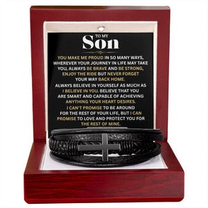 May include: A black leather bracelet with a silver cross is presented in an open wooden box. The box contains a message to "Son" with inspirational text. The box is red with a white interior.
