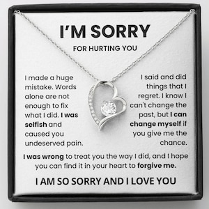 May include: A silver-toned heart-shaped pendant necklace with a central clear gemstone. The necklace is presented in a black box with the text "I'M SORRY" and a message of apology.