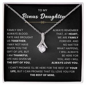 Peut inclure: Un collier pendentif en forme de ruban argenté avec une pierre ronde transparente centrale, présenté sur une carte noire avec le texte : TO MY Bonus Daughter, FAMILY ISN'T ALWAYS BLOOD. FATE HAS BROUGHT US TOGETHER. I AM THANKFUL THE GIFT OF YOU.