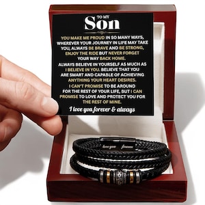 Op de afbeelding: Een zwarte gevlochten leren armband in een houten geschenkdoos. De doos bevat een kaart met de tekst "TO MY SON" en een liefdevolle boodschap. De armband heeft een magnetische sluiting met de tekst "love you forever".