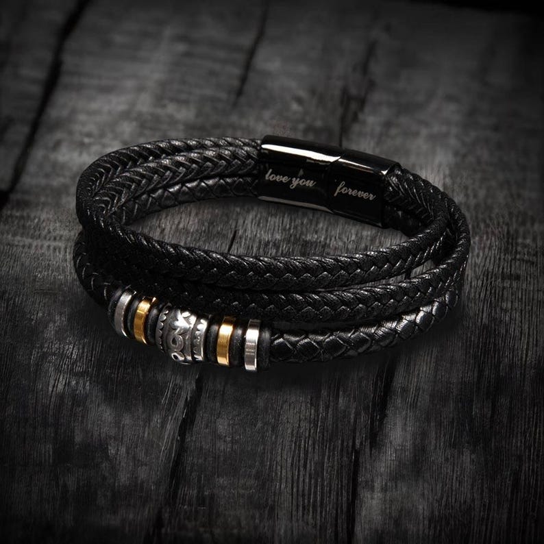 May include: Black leather wrap bracelet with braided strands and metallic accents. The bracelet features silver and gold-colored beads and a magnetic clasp engraved with "love you forever."