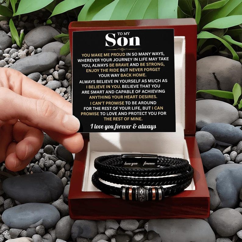 May include: A black leather bracelet with silver and copper accents is displayed inside a red wooden box. The box also contains a card with the text "TO MY SON" and a heartfelt message. The bracelet is a thoughtful gift.
