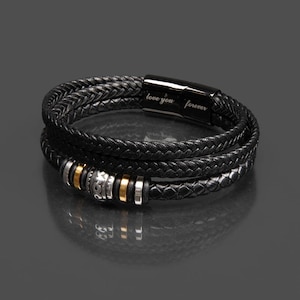 May include: Black braided leather bracelet with silver and gold accents. The bracelet has a magnetic clasp and the words "love you forever" are engraved on the clasp.