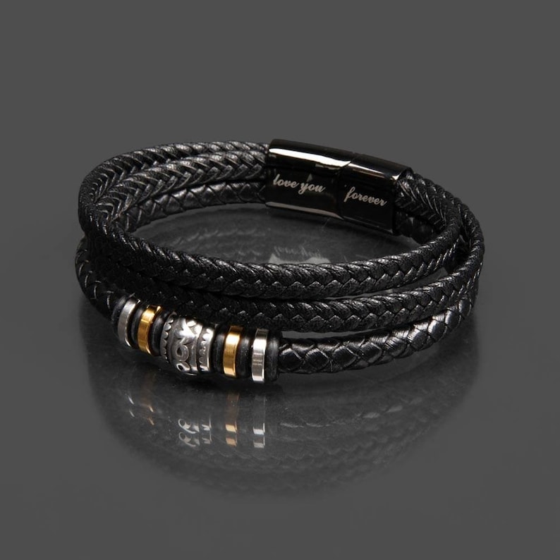 May include: Black braided leather bracelet with silver and gold accents. The bracelet has a magnetic clasp and the words "love you forever" are engraved on the clasp.
