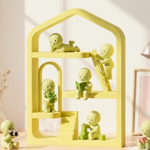 May include: A yellow decorative shelf unit with multiple levels, housing small, light green figurines in various poses. One figurine holds a camera, another reads a book, and others interact with blocks and a ladder. The text "Dymora3DPrints" is at the bottom.