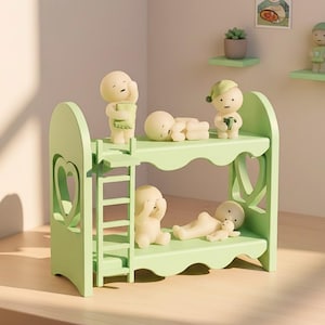 Op de afbeelding: Een lichtgroen stapelbed met een ladder, met verschillende kleine, cr&egrave;mekleurige beeldjes in verschillende poses. Het bed heeft hartvormige uitsparingen aan de zijkanten. Een klein plankje met beeldjes is zichtbaar op de achtergrond.
