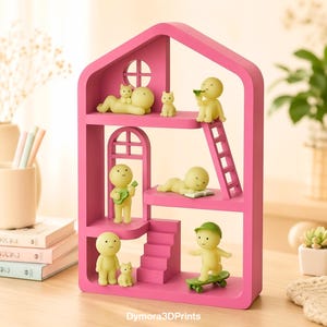 May include: A vibrant pink dollhouse-style shelf unit with several levels, populated by small yellow figurines engaged in activities like playing a guitar, reading, and skateboarding. Small cat figurines are also present. The unit is made of wood and rests on a wooden surface.