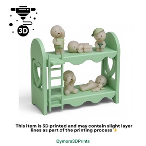 Op de afbeelding: Een lichtgroen 3D-geprint stapelbed met hartvormige uitsparingen. Kleine, gebroken witte beeldjes zijn op het bed geplaatst. De tekst "This item is 3D printed and may contain slight layer lines as part of the printing process" is zichtbaar.