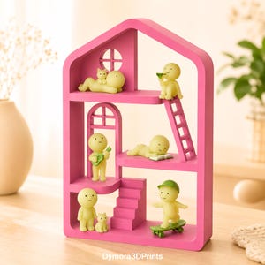 May include: A vibrant pink, house-shaped shelf unit with several levels, populated by small yellow figures. The figures are depicted in different poses, such as playing a guitar, skateboarding, and reading. A cat figurine is also included. The text "Dymora3DPrints" is visible.