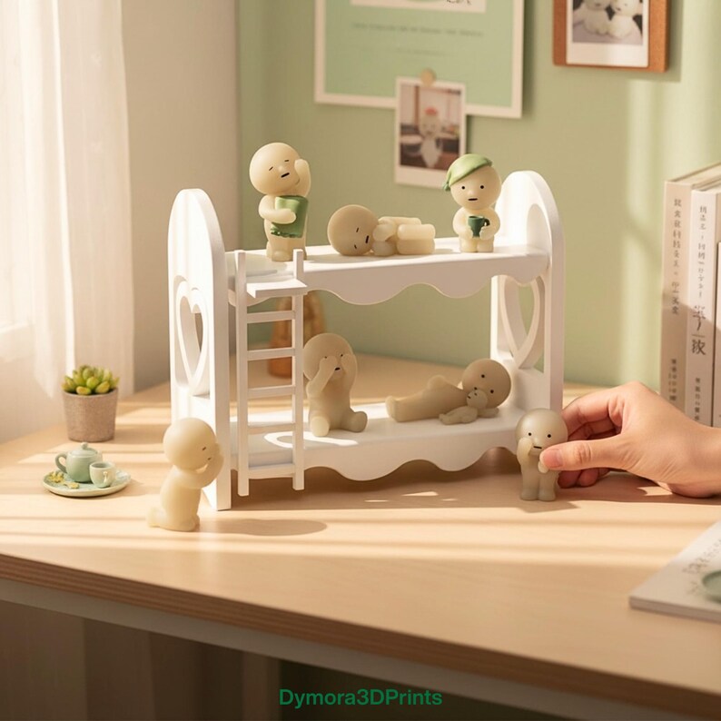 Op de afbeelding: Een wit stapelbed met hartvormige uitsparingen, met verschillende kleine, beige beeldjes in verschillende poses. Sommige beeldjes staan, andere liggen. Een kleine vetplant en een miniatuur theeservies staan op de tafel.