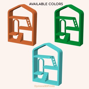 May include: Three 3D-printed miniature house-shaped shelves in orange, green, and blue. Each shelf has a staircase, ladder, and arched doorway. The text "AVAILABLE COLORS" is at the top. The text "Dymora3DPrints" is at the bottom.