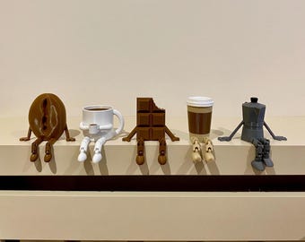 May include: A set of quirky figurines representing coffee and chocolate items. The collection features a coffee bean, a coffee cup, a chocolate bar with a bite missing, a takeaway coffee cup, and a stovetop espresso maker, each with arms and legs.