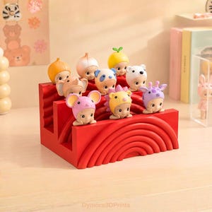 K&ouml;nnte beinhalten: Ein roter dekorativer Display-St&auml;nder h&auml;lt neun kleine Figuren, jede mit einem anderen Tierhut. Die Figuren sind in drei Reihen angeordnet. Zu den H&uuml;ten geh&ouml;ren ein B&auml;r, eine Giraffe, eine Maus und ein Igel. Der St&auml;nder hat ein geschwungenes Design.
