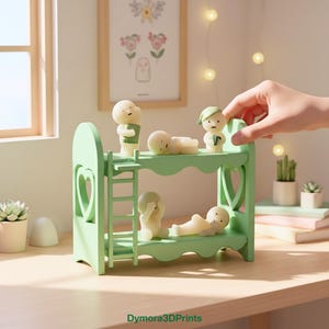 Op de afbeelding: Een lichtgroen stapelbed met hartvormige uitsparingen en een ladder, met verschillende kleine, bleke beeldjes. Een beeldje wordt door een hand op het bovenste bed geplaatst. De beeldjes bevinden zich in verschillende poses, sommige dragen kleine accessoires.