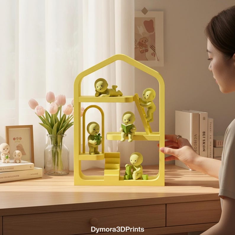 May include: A yellow, house-shaped shelf unit with multiple levels, featuring small, green figurines in various poses. The figurines are arranged on the shelves, some reading, climbing a ladder, or holding objects. The text "Dymora3DPrints" is visible at the bottom.
