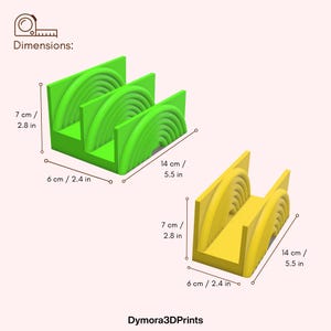 K&ouml;nnte beinhalten: Zwei 3D-gedruckte Halterungen, eine gr&uuml;ne und eine gelbe, mit einem geschichteten Design. Der gr&uuml;ne Halter misst 6 cm x 14 cm x 7 cm, w&auml;hrend der gelbe die gleichen Abmessungen hat. Der Text "Dymora3DPrints" steht unten.