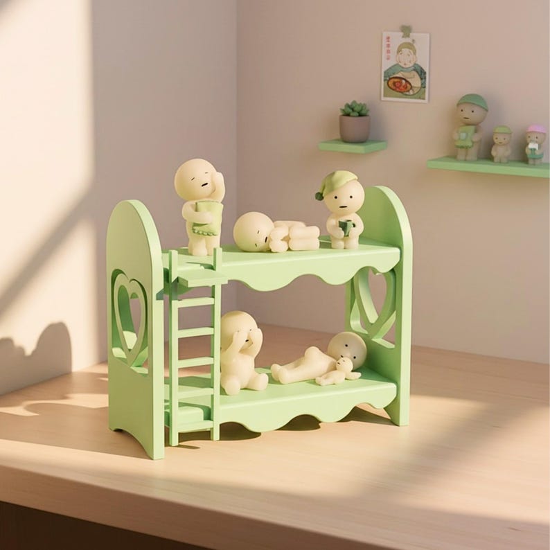 Op de afbeelding: Een lichtgroen stapelbed met een ladder, met verschillende kleine, cr&egrave;mekleurige beeldjes in verschillende poses. Het bed heeft hartvormige uitsparingen aan de zijkanten. Een klein plankje met beeldjes is zichtbaar op de achtergrond.