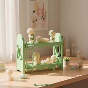 Op de afbeelding: Een lichtgroen stapelbed met hartvormige uitsparingen en een ladder, bevolkt met kleine, gebroken witte beeldjes in verschillende poses. Sommige beeldjes staan, andere liggen. De sc&egrave;ne speelt zich af op een houten oppervlak.