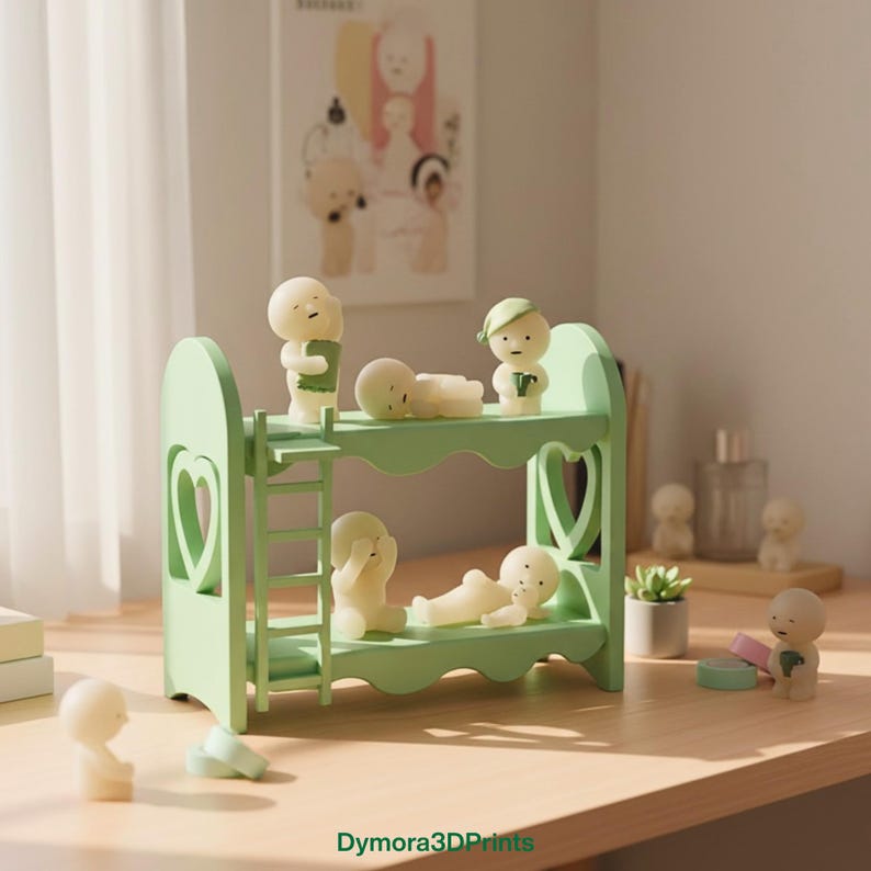 Op de afbeelding: Een lichtgroen stapelbed met hartvormige uitsparingen en een ladder, bevolkt met kleine, gebroken witte beeldjes in verschillende poses. Sommige beeldjes staan, andere liggen. De sc&egrave;ne speelt zich af op een houten oppervlak.