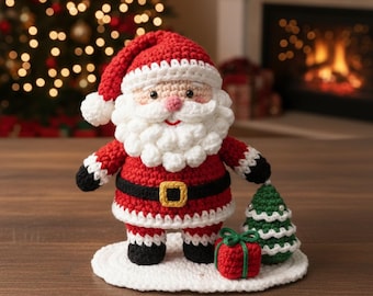 May include: A crocheted Santa Claus figure in a red suit with a white beard and hat. The figure has a black belt with a gold buckle and is holding a small green Christmas tree. A red gift box is also present.