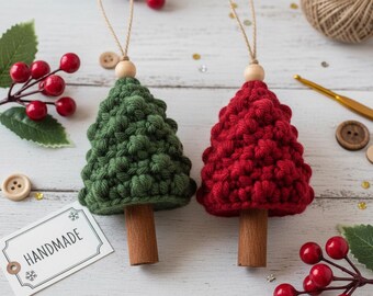 Op de afbeelding: Twee handgemaakte gehaakte kerstboomornamenten. De ene is groen, de andere is rood. Elke boom heeft een houten stam, een houten kraal aan de bovenkant en een touwlus om op te hangen. Het label luidt "HANDMADE".
